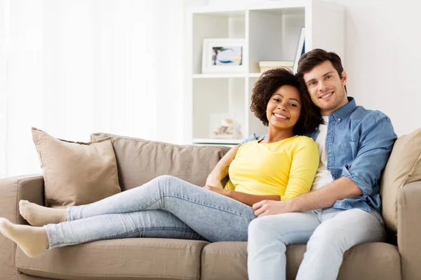 Boldog mosolygó nemzetközi pár otthon a kanapén — Stock Fotó