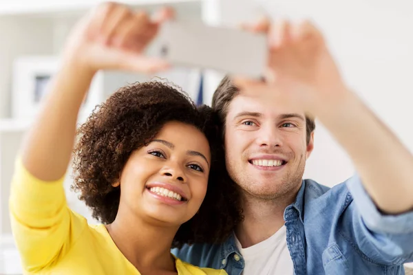 Casal feliz com smartphone levando selfie em casa — Fotografia de Stock