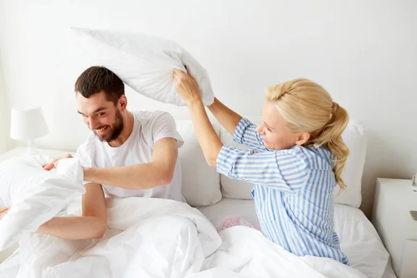 Feliz pareja teniendo almohada lucha en cama en casa —  Fotos de Stock