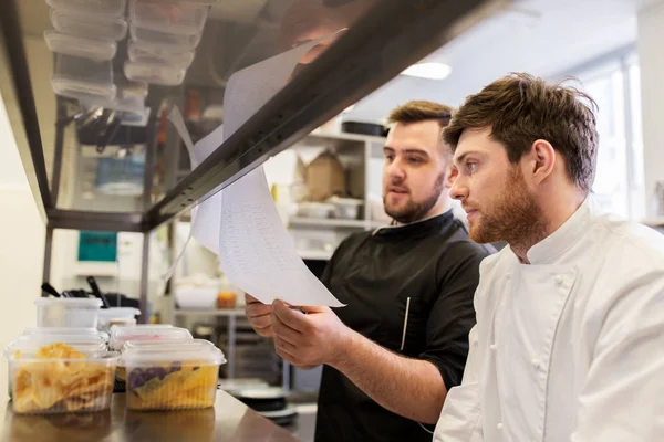 Chef e cozinheiro com listas ou contas na cozinha — Fotografia de Stock