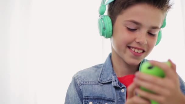 Niño feliz con teléfono inteligente y auriculares en casa — Vídeos de Stock