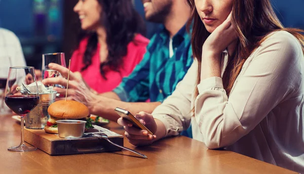 Vrouw met smartphone en vrienden op restaurant — Stockfoto