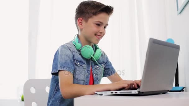 Menino feliz com fones de ouvido digitando no laptop em casa — Vídeo de Stock