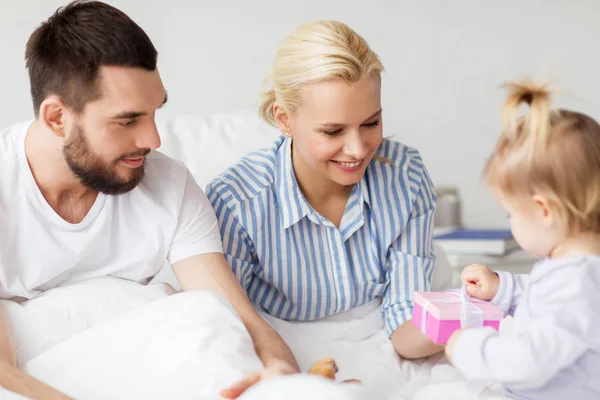 Família feliz com caixa de presente na cama em casa — Fotografia de Stock