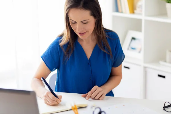 Lycklig kvinna skriver till anteckningsboken på kontor — Stockfoto