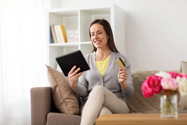 Mujer feliz con tablet PC y tarjeta bancaria en casa — Foto de Stock