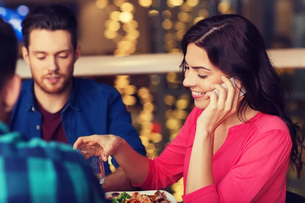 Kvinna med smartphone och vänner på restaurang — Stockfoto