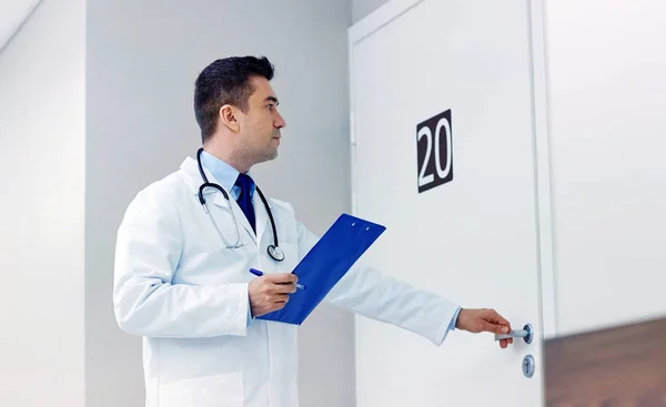 Doctor with clipboard opening hospital ward door — Stock Photo, Image