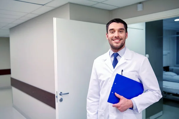 Happy doctor with clipboard at hospital corridor — Stock Photo, Image