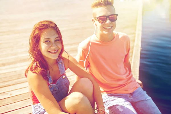 Happy teenage couple with earphones on river berth — Stock Photo, Image