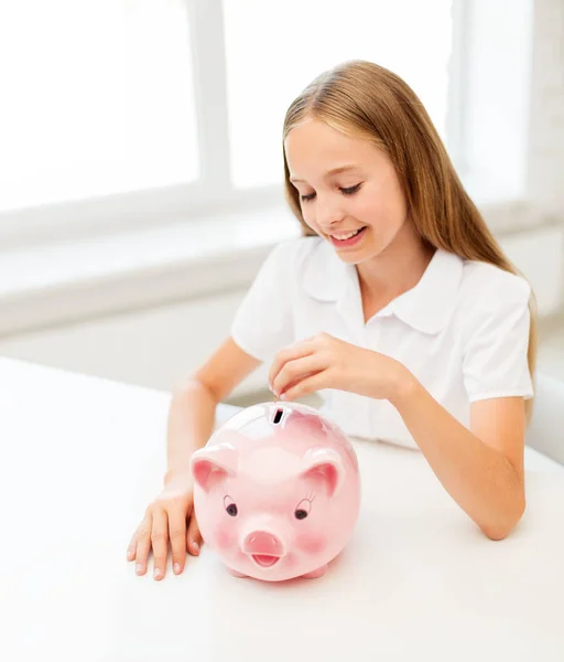 Feliz sorrindo menina colocando moeda em porquinho banco — Fotografia de Stock