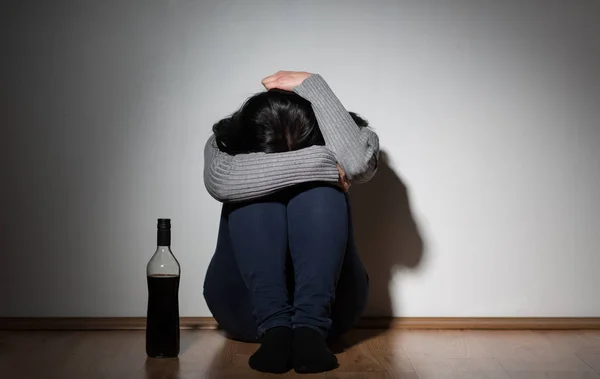 Жінка з пляшкою алкоголю плаче вдома — стокове фото