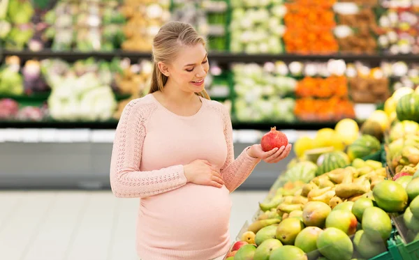 Mujer embarazada feliz con granada en el supermercado —  Fotos de Stock
