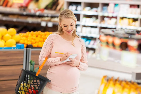 Pregnant woman with shopping basket at grocery — Stock Photo, Image