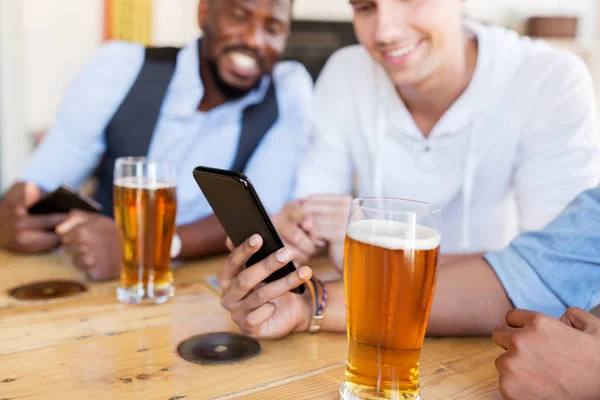 Kamarády s smartphone, pití piva na baru — Stock fotografie