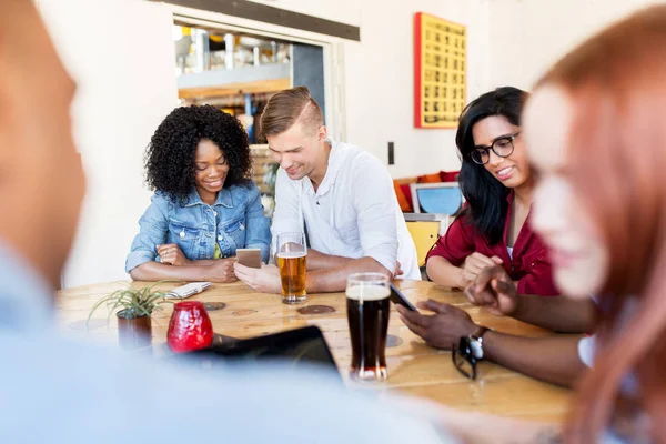 Счастливые друзья со смартфоном пьют пиво в баре — стоковое фото