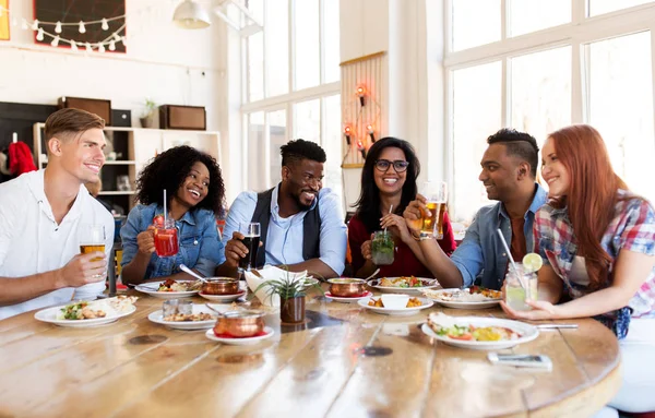 Amigos felizes comendo e bebendo no restaurante — Fotografia de Stock