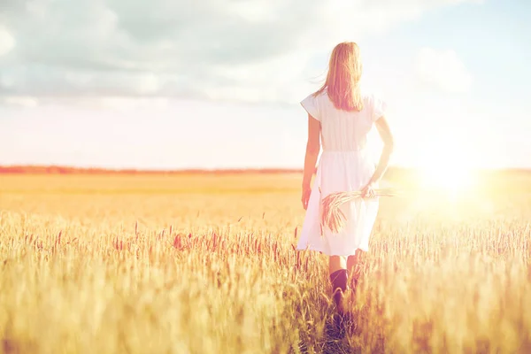 Mujer joven con espiguillas de cereales caminando en el campo — Foto de Stock