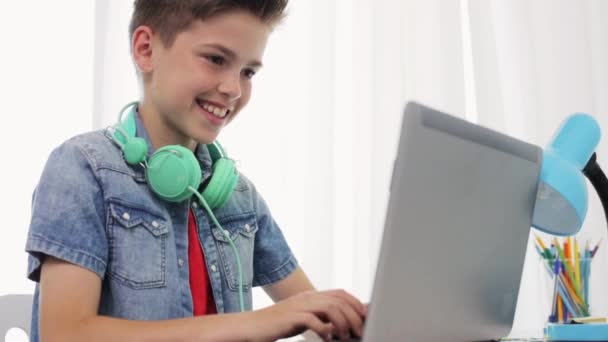 Niño feliz con auriculares escribiendo en el ordenador portátil en casa — Vídeos de Stock