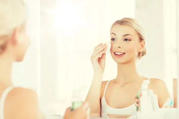 Junge Frau mit Lotion wäscht Gesicht im Badezimmer — Stockfoto