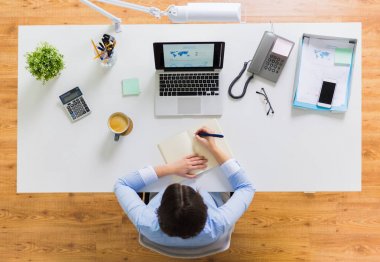 businesswoman writing to notebook at office clipart