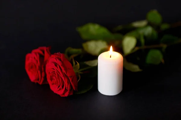 Красные розы и горящая свеча на черном фоне — стоковое фото