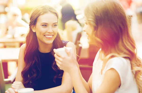 Smiling young women with coffee cups at cafe — Stock Photo, Image