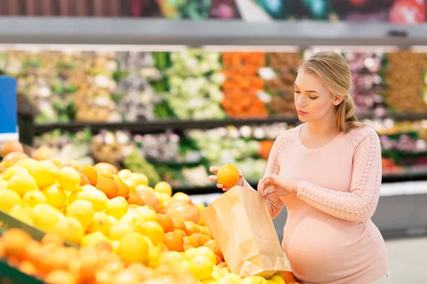 Mujer embarazada con bolsa de comprar naranjas en la tienda de comestibles — Foto de Stock