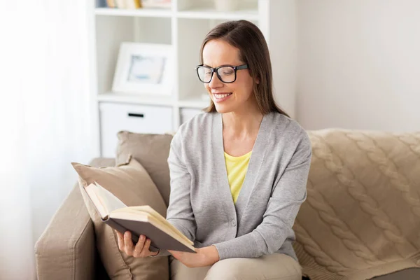 Giovane donna in occhiali lettura libro a casa — Foto Stock