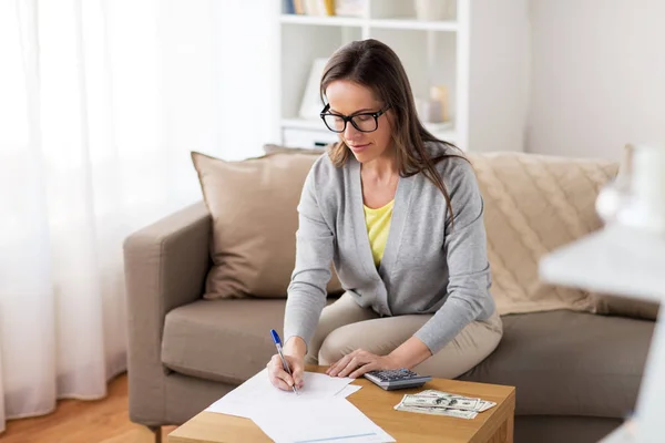 Mujer con dinero, papeles y calculadora en casa — Foto de Stock