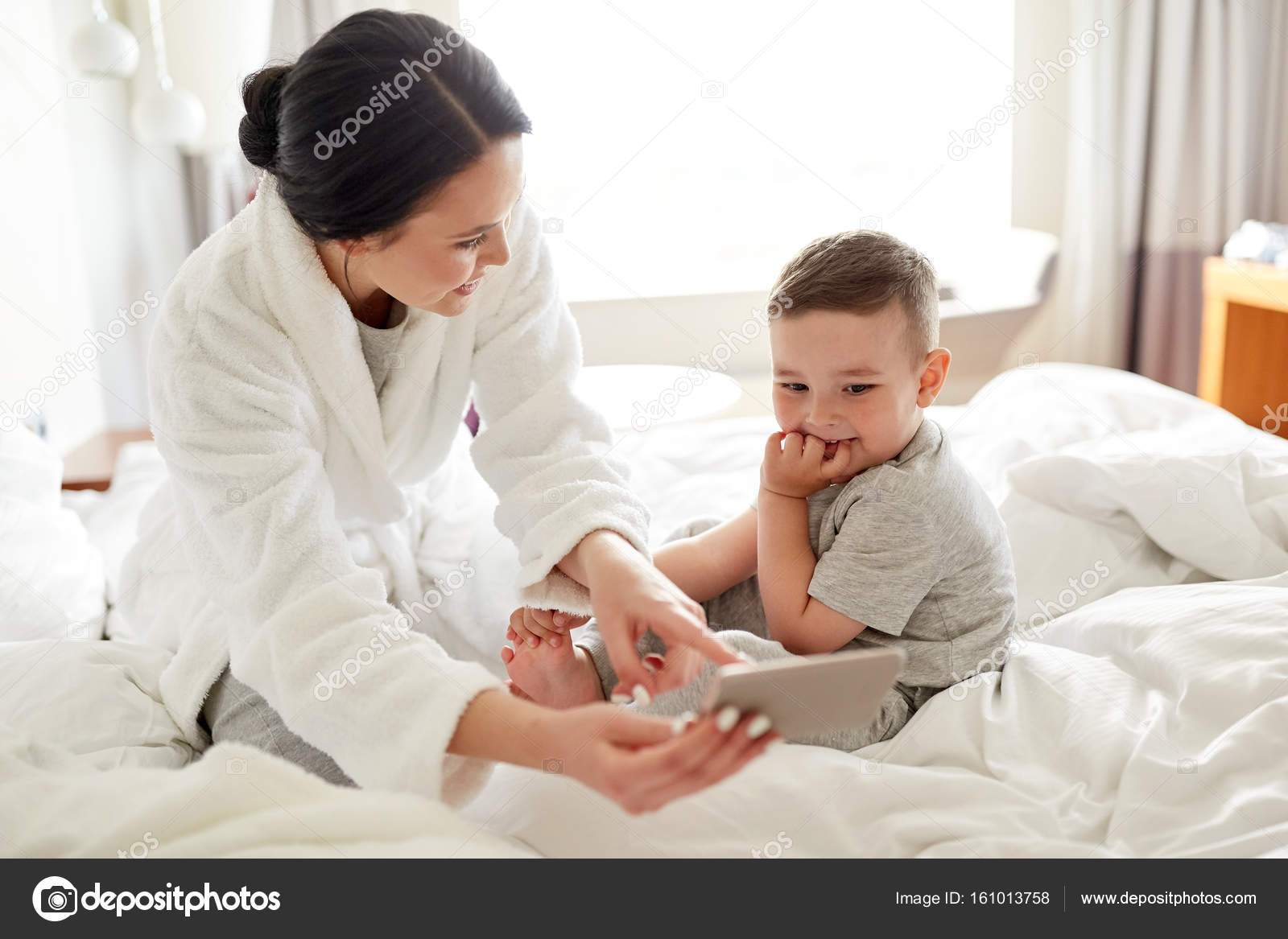 Mother And Son With Smartphone In Bed At Hotel Stock Photo