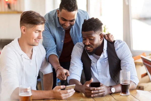 Amigos masculinos com smartphone bebendo cerveja no bar — Fotografia de Stock