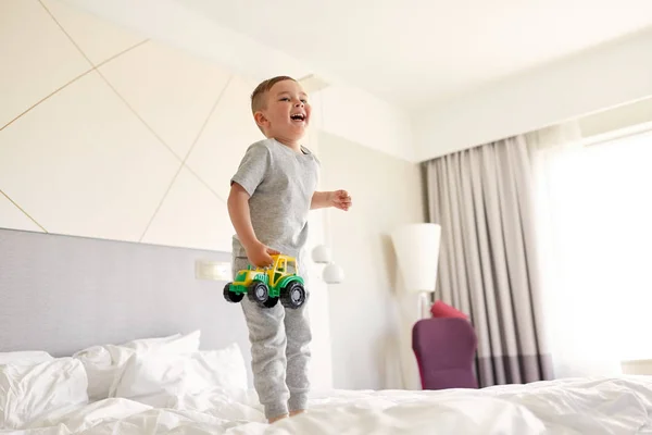 Glücklicher kleiner Junge mit Spielzeugauto zu Hause oder im Hotelbett — Stockfoto