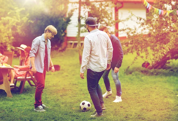 Счастливые друзья играют в футбол в летнем саду — стоковое фото