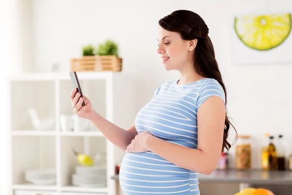 Gelukkig zwanger vrouw met smartphone in keuken — Stockfoto