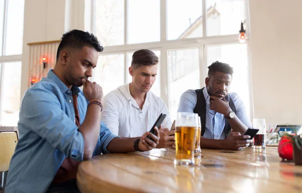 Amigos masculinos com smartphone bebendo cerveja no bar — Fotografia de Stock