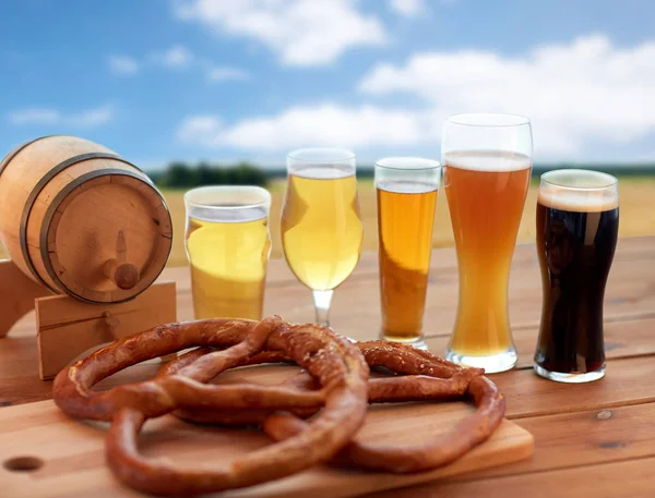 Vasos de cerveza, barril y pretzel sobre el campo de cereales — Foto de Stock