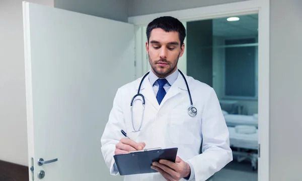Doctor writing to clipboard at hospital — Stock Photo, Image