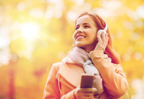 智能手机和耳机在秋天的公园里的女人 — 图库照片
