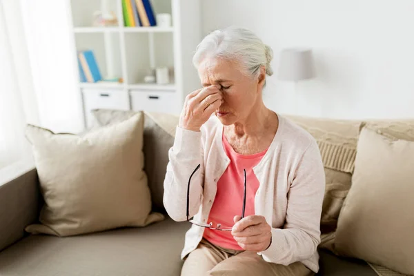 Пожилая женщина в очках с головной болью дома — стоковое фото