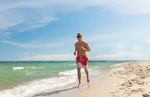 Homme heureux avec écouteurs courir le long de la plage — Photo