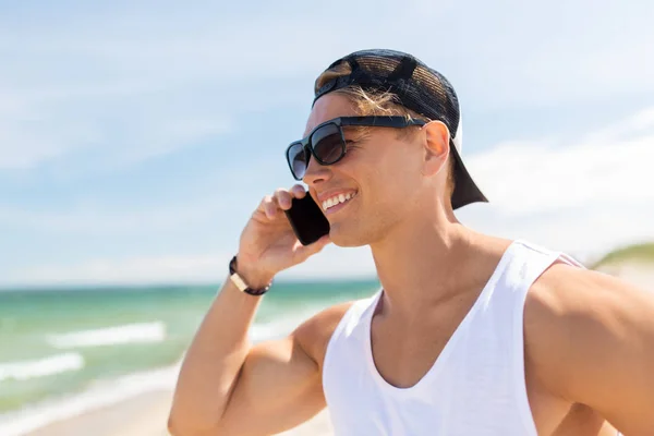 Улыбчивый мужчина звонит по смартфону на летнем пляже — стоковое фото