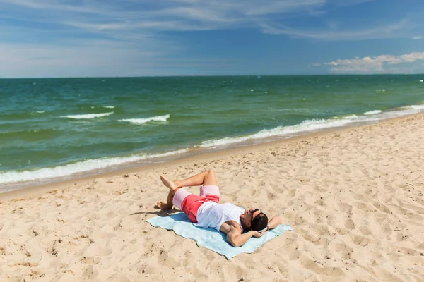 Lyckligt leende ung man sola på strandhandduk — Stockfoto