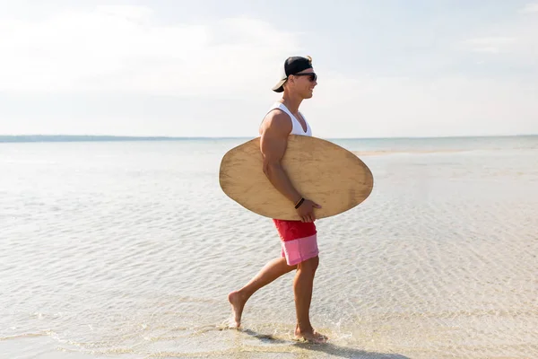 Счастливый молодой человек со скимбордом на летнем пляже — стоковое фото