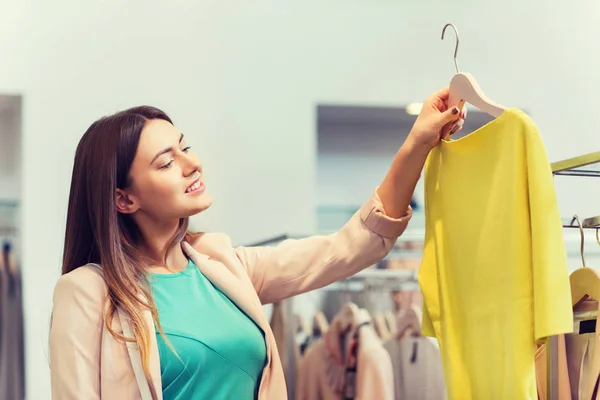 Mutlu genç kadın alışveriş merkezinde giysiler seçmek — Stok fotoğraf