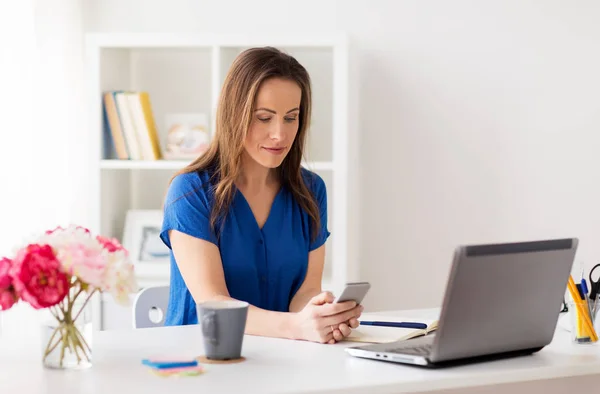Женщина со смартфоном и ноутбуком в офисе — стоковое фото