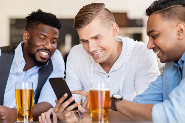 Amigos masculinos com smartphone bebendo cerveja no bar — Fotografia de Stock