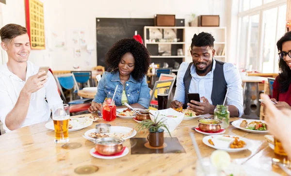 Amici felici con gli smartphone al ristorante — Foto Stock