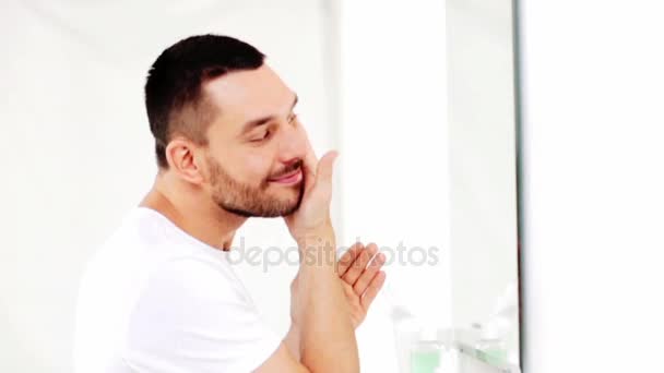 Hombre feliz aplicando aftershave a cara en el baño — Vídeo de stock