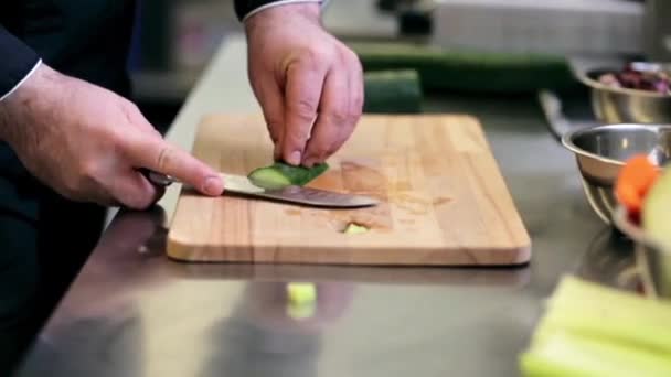 Руки повара мужского пола, рубящего огурец на кухне — стоковое видео